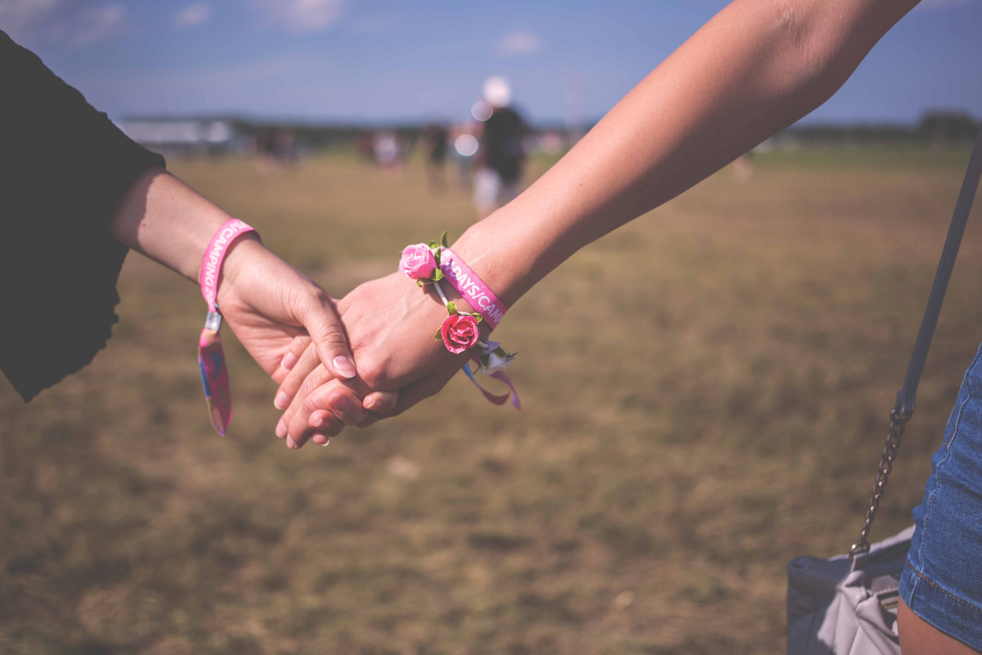 Close up of two people wearing pink wristbands holding hands