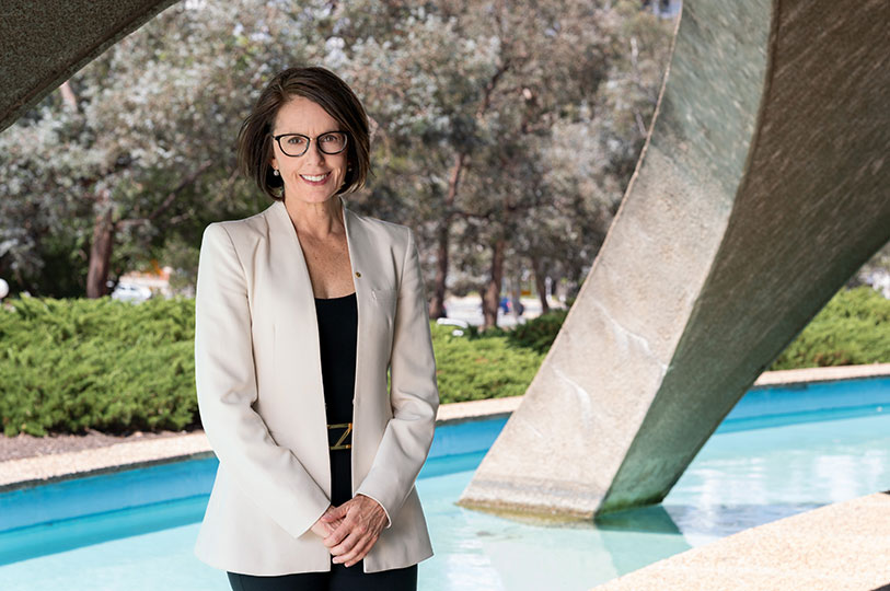 Anna-Maria Arabia stands under the arches of the Shine Dome next to the blue water of the moat. She is smiling.