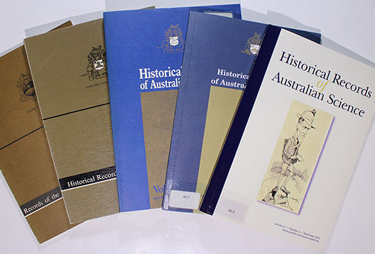 Five different covers of the Historical Records of Australian Science laid out, with the two earlier editions brown in colour, the next two blue, and the most recent one white.