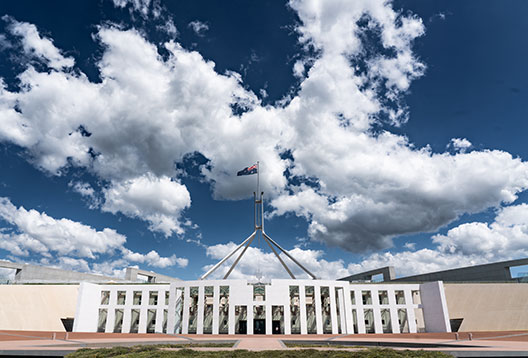 Australia's Parliament House in Canberra with the flag flying against a blue sky with fluffy white clouds
