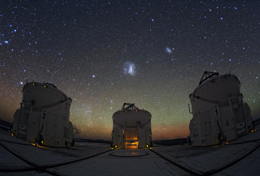 Three large telescope buildings under a starry night sky.