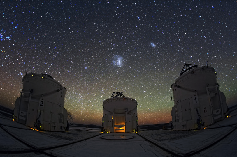 Three large telescope buildings at night underneath a starry sky