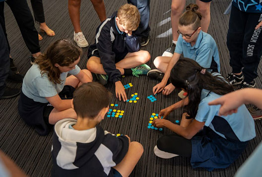 Five kids sitting inside in a circle engrossed in an activity with bright coloured counters