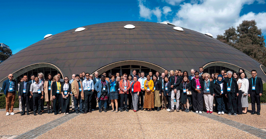 A large group of people stand for a group photo outside the Shine Dome on a sunny blue-sky day