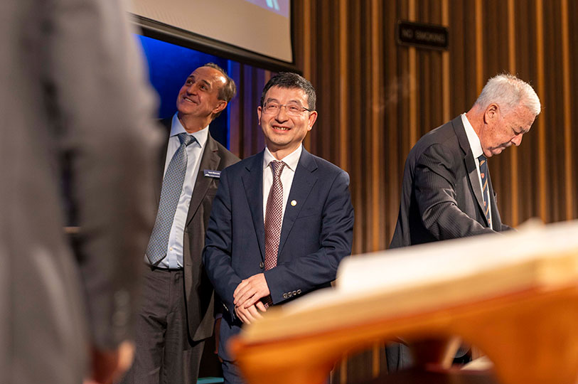 A man smiles broadly as he approaches a large open book on a podium.