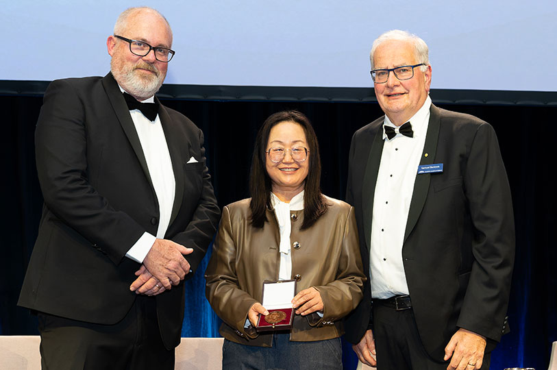 Professor Zaiping Guo shows off a medal in a case while standing with Minister for Science Senator Tim Ayres and Academy President Professor Sam Berkovic
