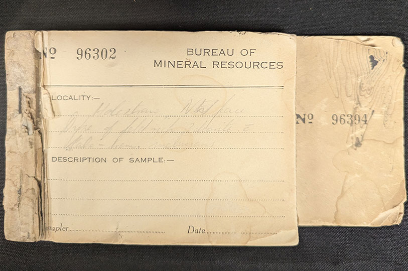 A faded, yellowed booklet bound with a staple, and with some pages ripped out like a cheque book. The book has the number 96302 printed on it alongside 'Bureau of Mineral Resources'. Labelled lines for entries include: Locality, Description of Sample, Sampler and Date. The page is partially filled out with cursive pencil handwriting.