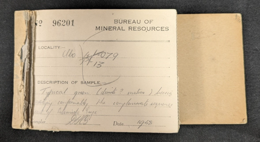A close-up of a faded, yellowed booklet with some pages removed (like a cheque book). The page is printed with a number '96201' and the words 'Bureau of Mineral Resources', alongside labelled lines for entries: Locality, Description of sample, Sampler and Date. The top page is filled out with cursive pencil handwriting.