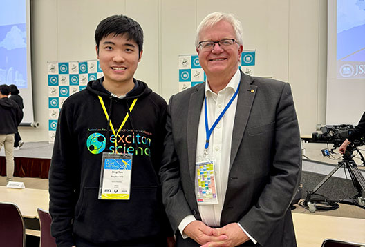 Dr Dingchen Wen and Professor Brian Schmidt pose for a photo together. Both are smiling and wearing conference lanyards.