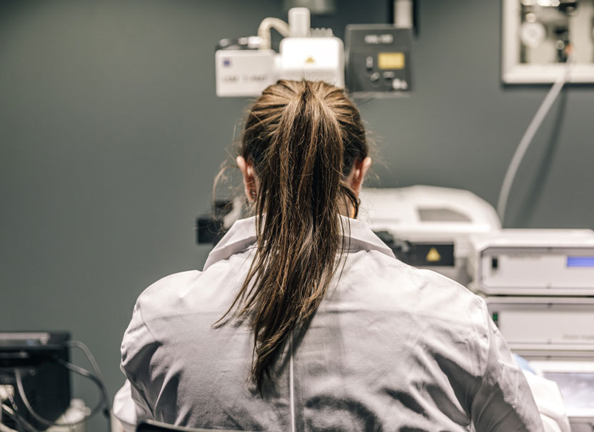 A person with long hair wearing a labcoat faces away from the camera.