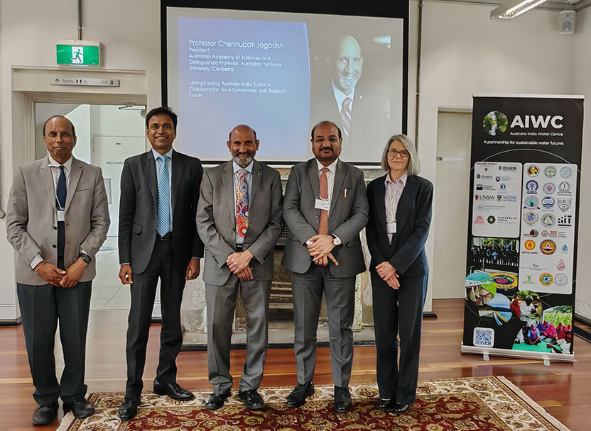 Five people dressed in formal business attire stand in a line in front of a projector screen