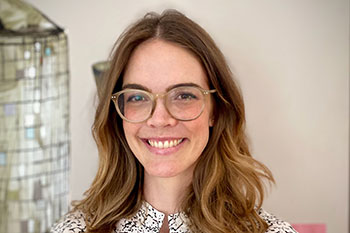 A woman with shoulder length brown hair and glasses smiles at the camera.
