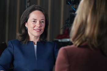 A woman with shoulder length brown hair is interviewed on camera