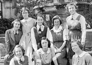Group of eight teenage girls in school uniform smiling and looking relaxed (black and white photo)